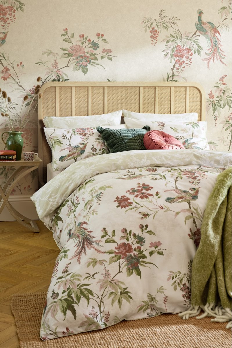 Light and bright scheme with wall panelling, rattan bed, patterned linen, and green and pink decor.