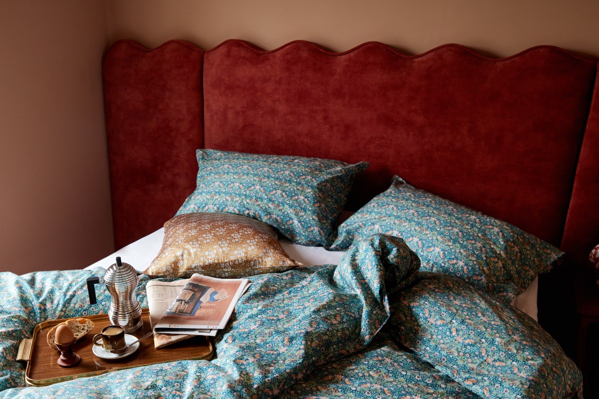 Bedroom with rust velvet bed, teal bedding and a breakfast tray.