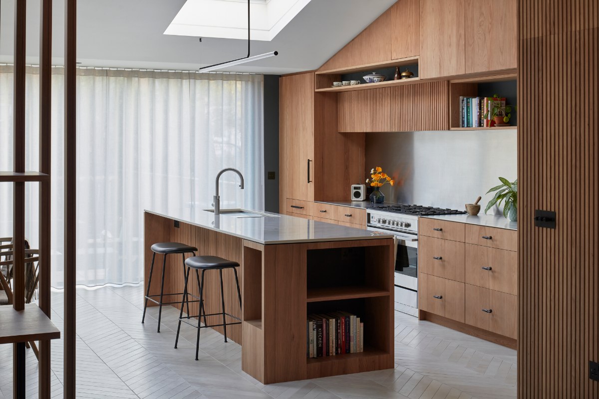 Wood kitchen with drawers, fluted finishes, open shelving, and a central multi-functional unit with sink and tap.