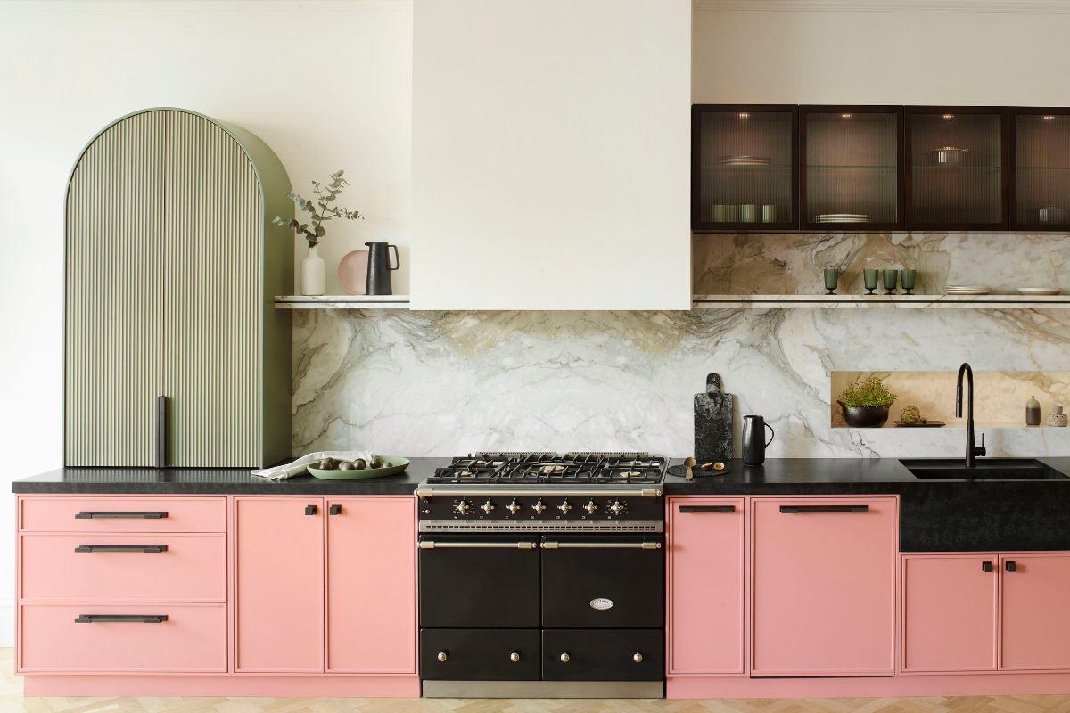 Modern kitchen design with pink cabinetry, a green reeded cupboard, stone splashback and dark worktops.