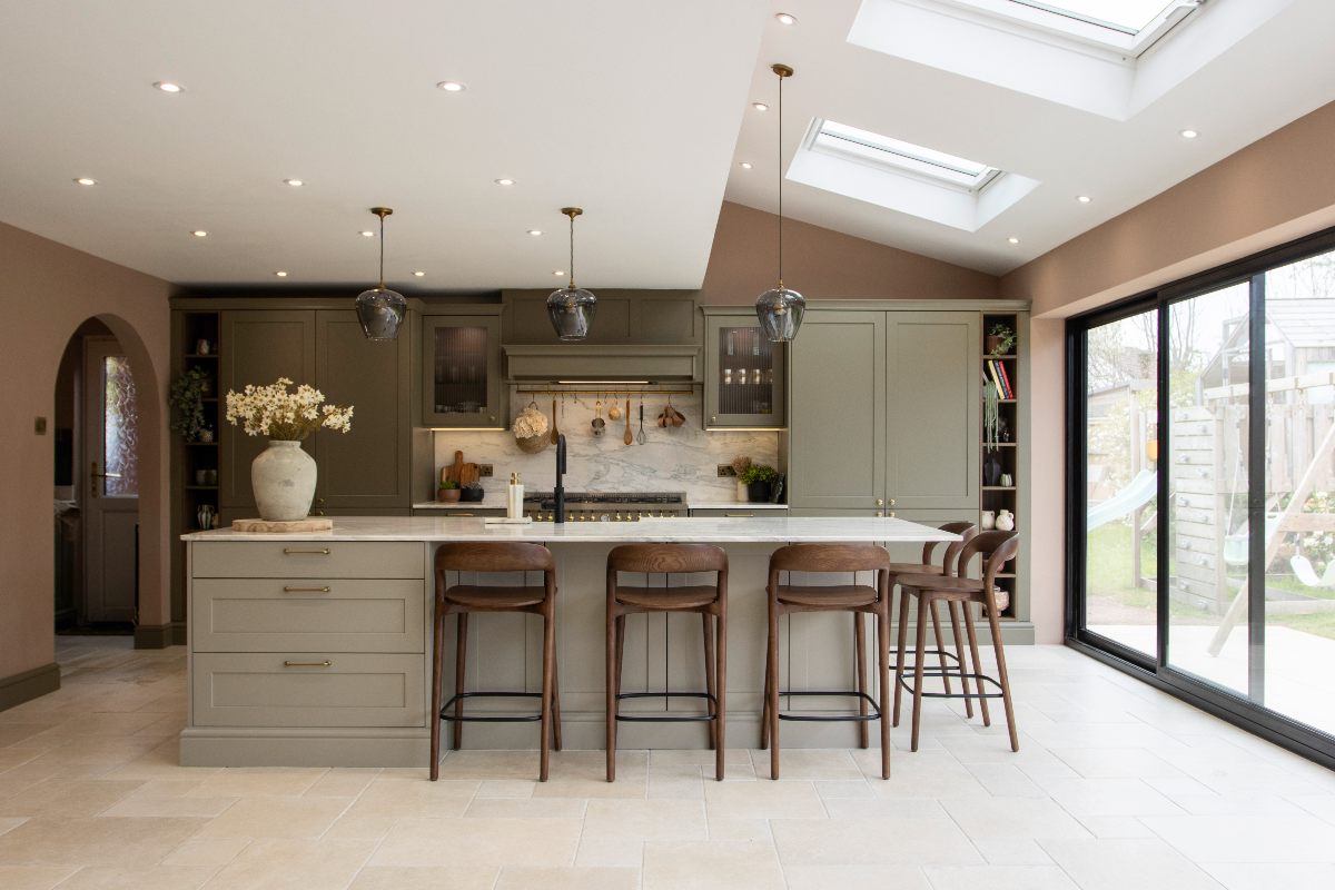 Sage green kitchen with a multi-functional island, glazing, and layered lighting.