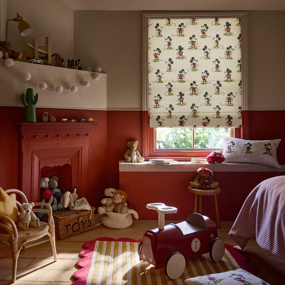 Kids bedroom with Mickey Mouse blinds, cushions, red wall paint, and striped furnishings.