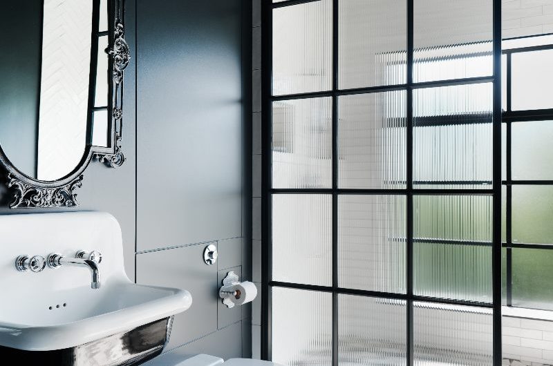A bathroom design with a walk-in shower, patterned flooring and industrial elements such as steel-framed shower panel and metallic basin.