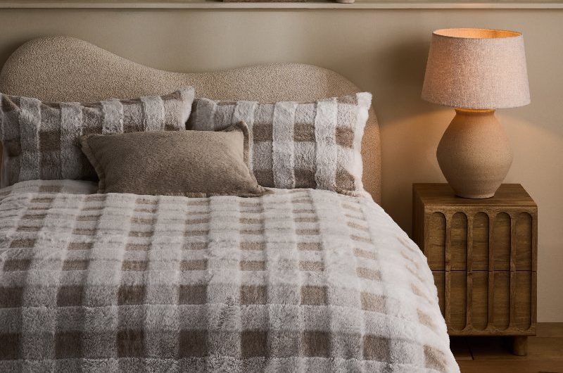 Cosy bedroom with a boucle bed frame, faux fur bedding, wood bedside table and table lamp.