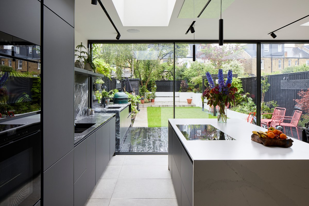A handleless kitchen design with a glass door, island with hob, and skylight.