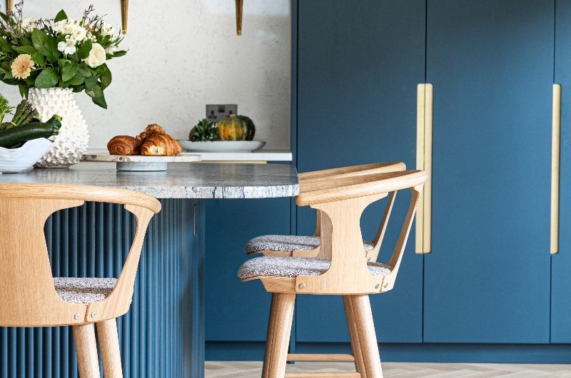 A vibrant blue design with wood accents, marbled worktop and splashbacks and an open shelf for storage. 