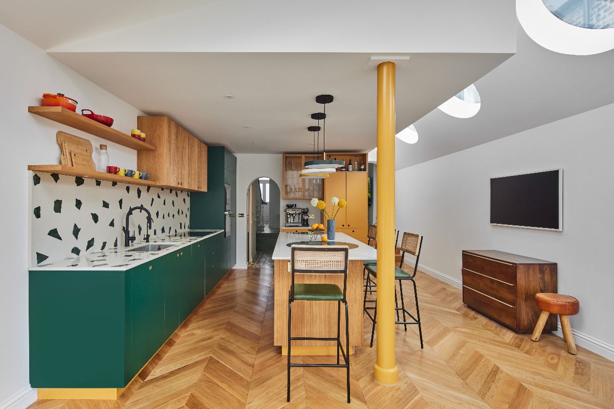 Green kitchen design with wood and mustard cabinets, a yellow beam, and wood flooring.