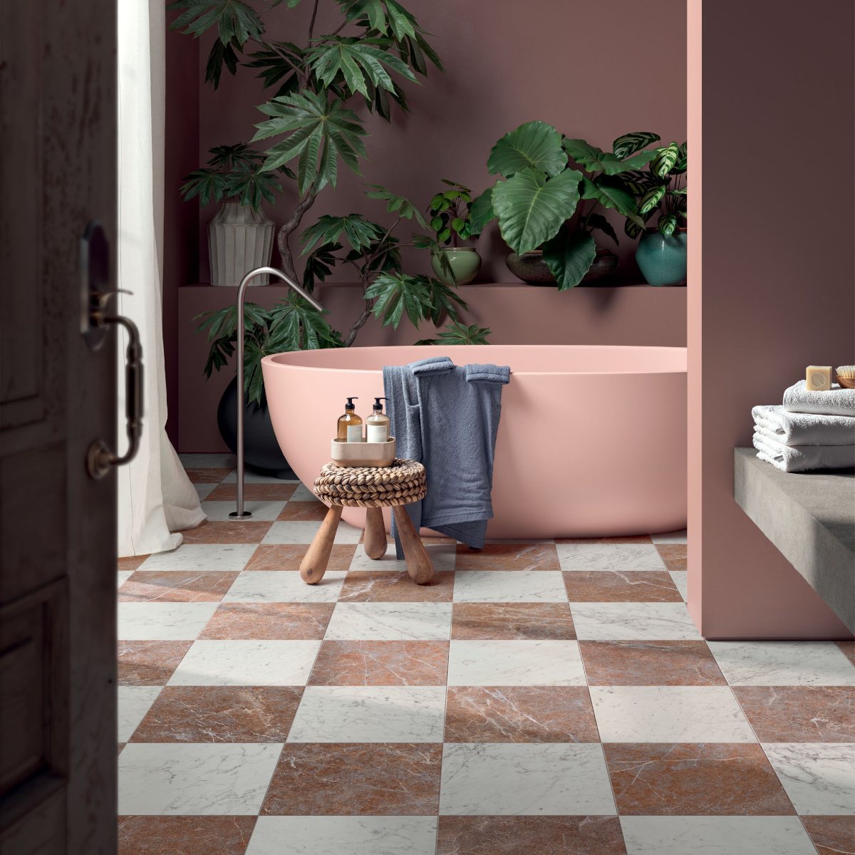 Pink bathroom with a painted tub, checkered flooring and house plants.