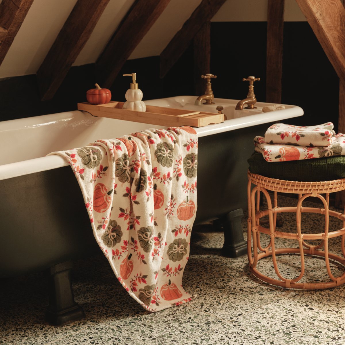 Autumnal bathroom with wood beams, pumpkin-printed towels, a green freestanding tub, and pumpkin-shaped accessories.