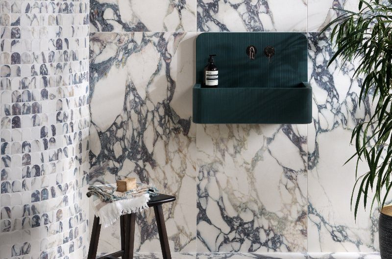 Bathroom clad in marble slabs, with a curved wall, and wall-mounted green basin and oval mirror.