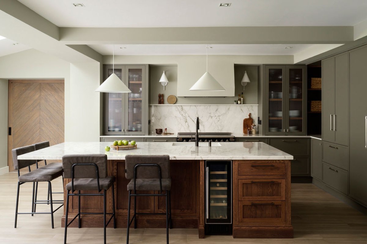 L-shaped island with bar stools, sink and tap, and storage in a green kitchen.