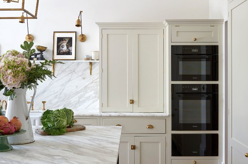 Kitchen design with neutral, classic cabinetry and a dark island topped with marble surfaces.