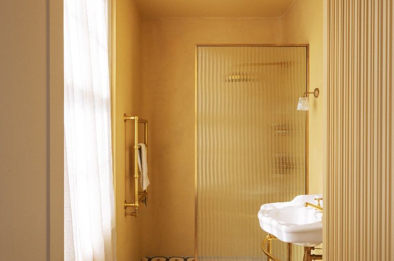 A yellow drenched shower room with classic basin, gold brassware and patterned flooring.