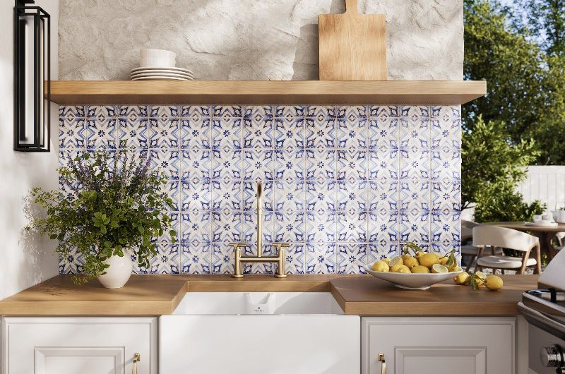 A Mediterranean-inspired washing up area with blue and white tiles, a sink and tap, wood worktop and open shelving.
