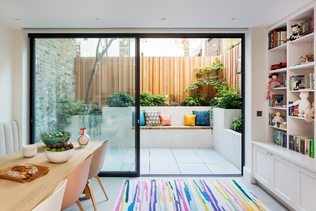 A kitchen with a table and chairs leading onto the garden with a compact seating spot.