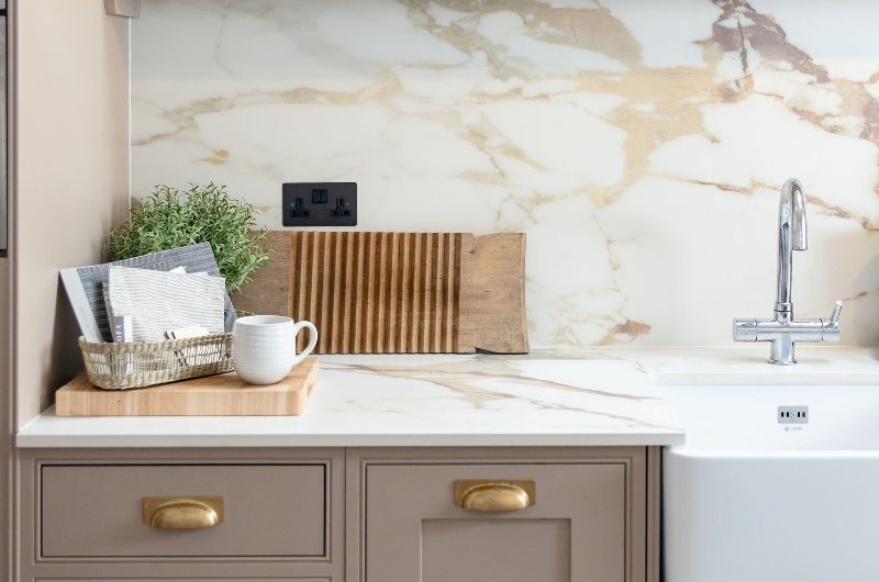 Classic Shaker kitchen with gold hardware, veiny surfaces, and an open shelf for decorations.