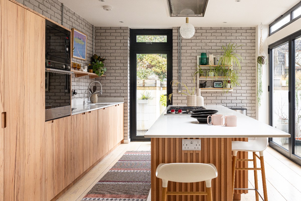 A wood kitchen design with a run of cabinets with built-in appliances and sink and tap, plus a fluted island with seating and a gas hob.