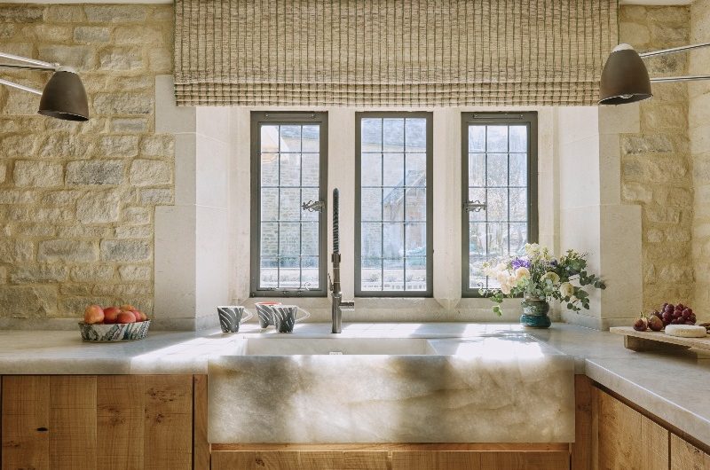 Sink zone with wood cabinetry, a stone bowl and matching work surfaces by a window which floods the room with light.