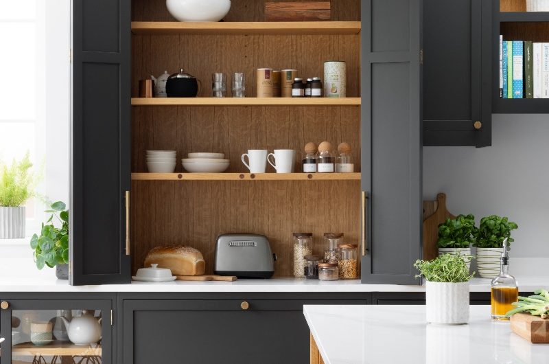 An open breakfast cupboard with wood interiors in a dark grey kitchen design with a matching wood island.