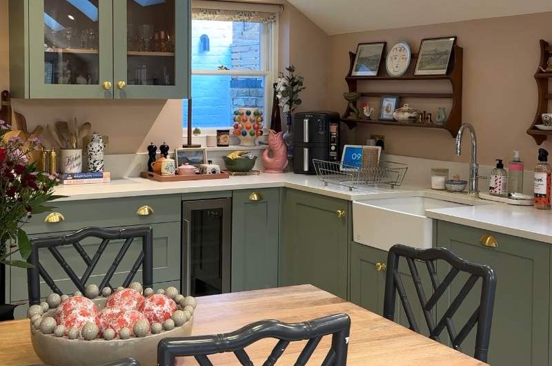 A kitchen renovation with green cabinets, wood table and black chairs, and natural lighting.