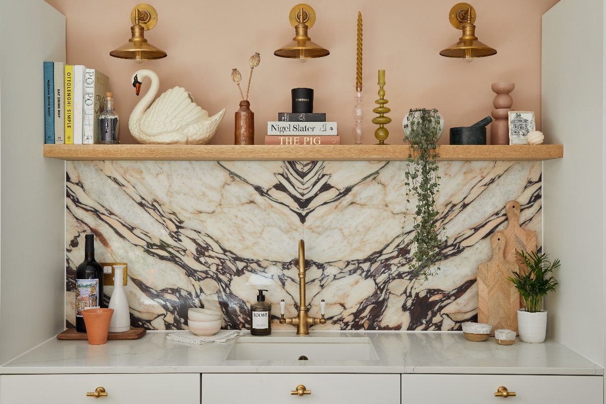 A sink zone with marble splashback, white surfaces, an inset sink, classic tap, wood shelf with decorations, and sleek white cabinetry.