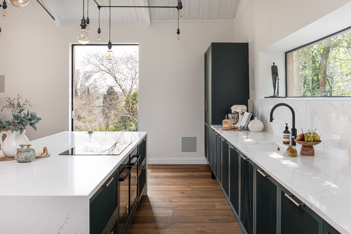 View of the galley kitchen layout with a central island, with built-in appliances, and white work surfaces.