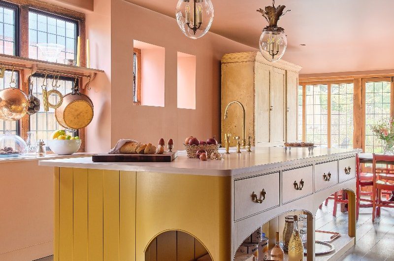 A yellow freestanding island in a pale pink room with striking lighting and big windows.