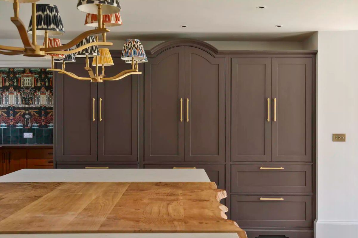 Painted Shaker cabinets in a dark brown with gold hardware disguising a fridge, a pantry, and drinkware storage.