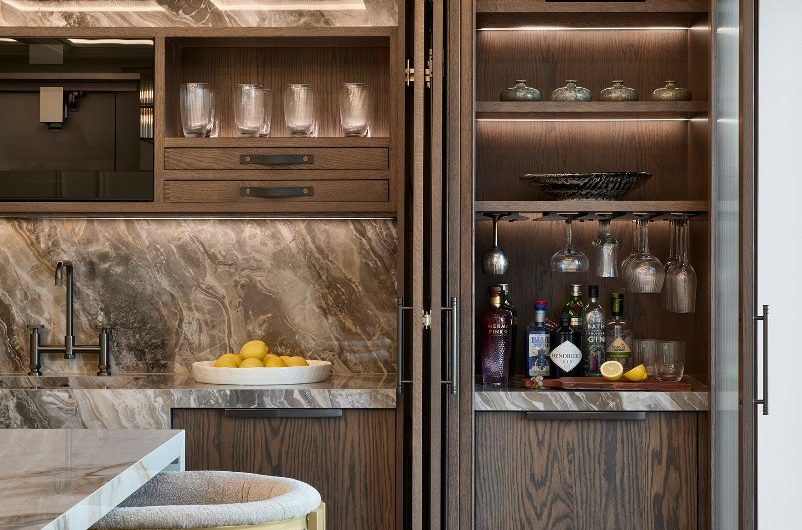 Sophisticated kitchen design with grainy wood cabinetry, statement marble, bar area, coffer ceiling with LED lighting, and a luxury island.