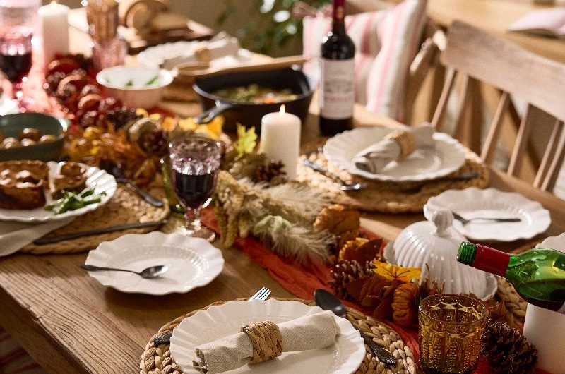 An autumn table scheme with rattan placemats, white textured crockery, a seasonal garland, and coloured wine glasses.