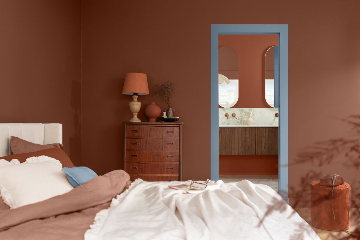 A calming bedroom scheme drenched in a warm terracotta colour, with pale blue on the woodwork leading to the bathroom.