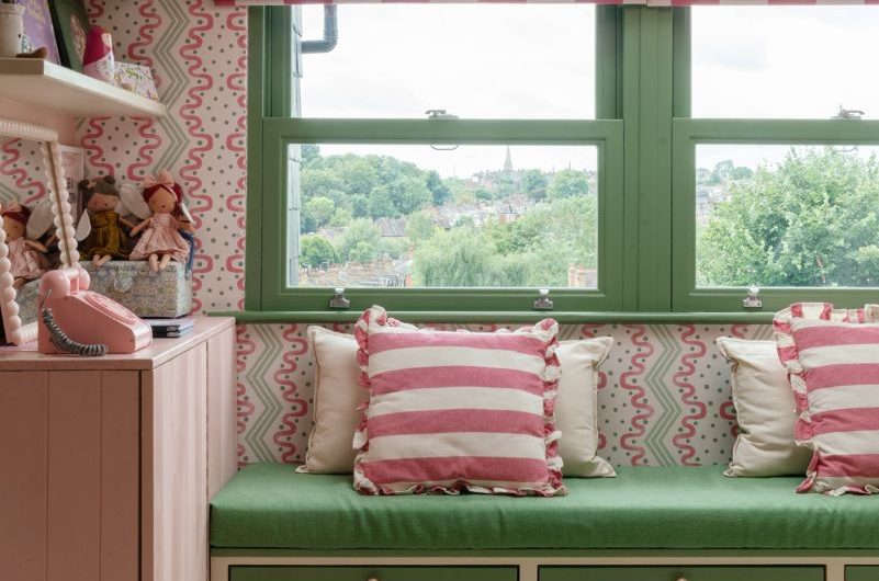 Window nook with green seating, green drawers, patterned wallpaper, and matching green window frames.