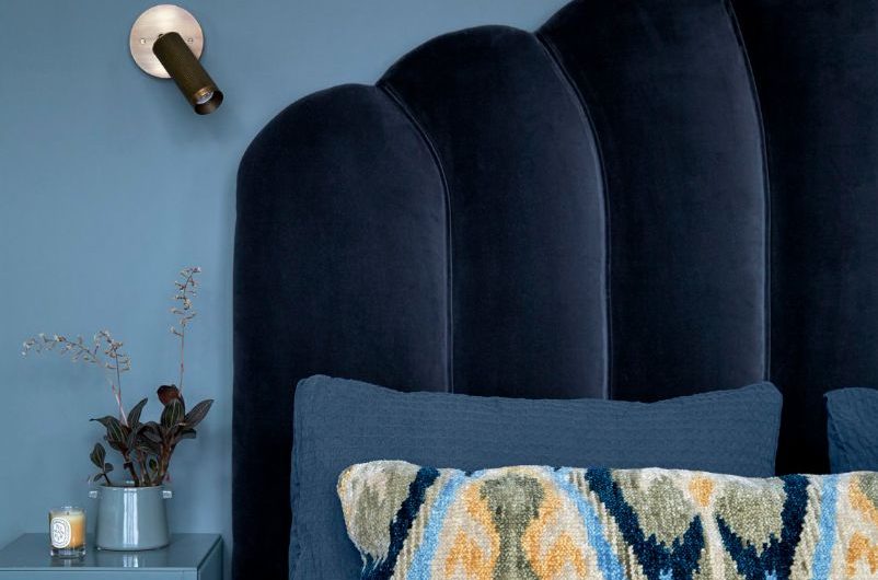 Blue bedroom design with a velvet bed frame and wall-mounted light and beside table.