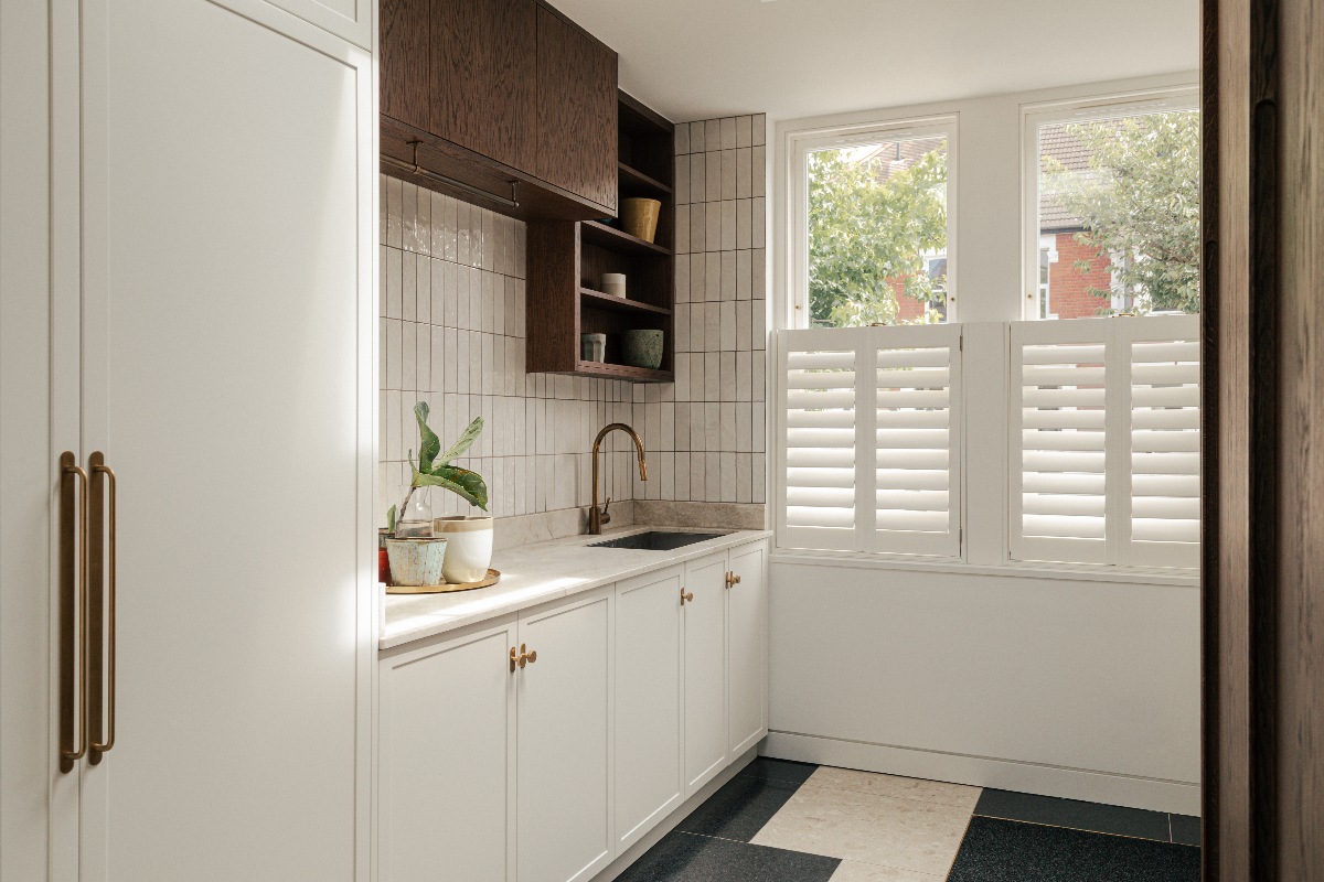 A white utility room with metro tiles, white cabinets, wood wall units, and white shutters.