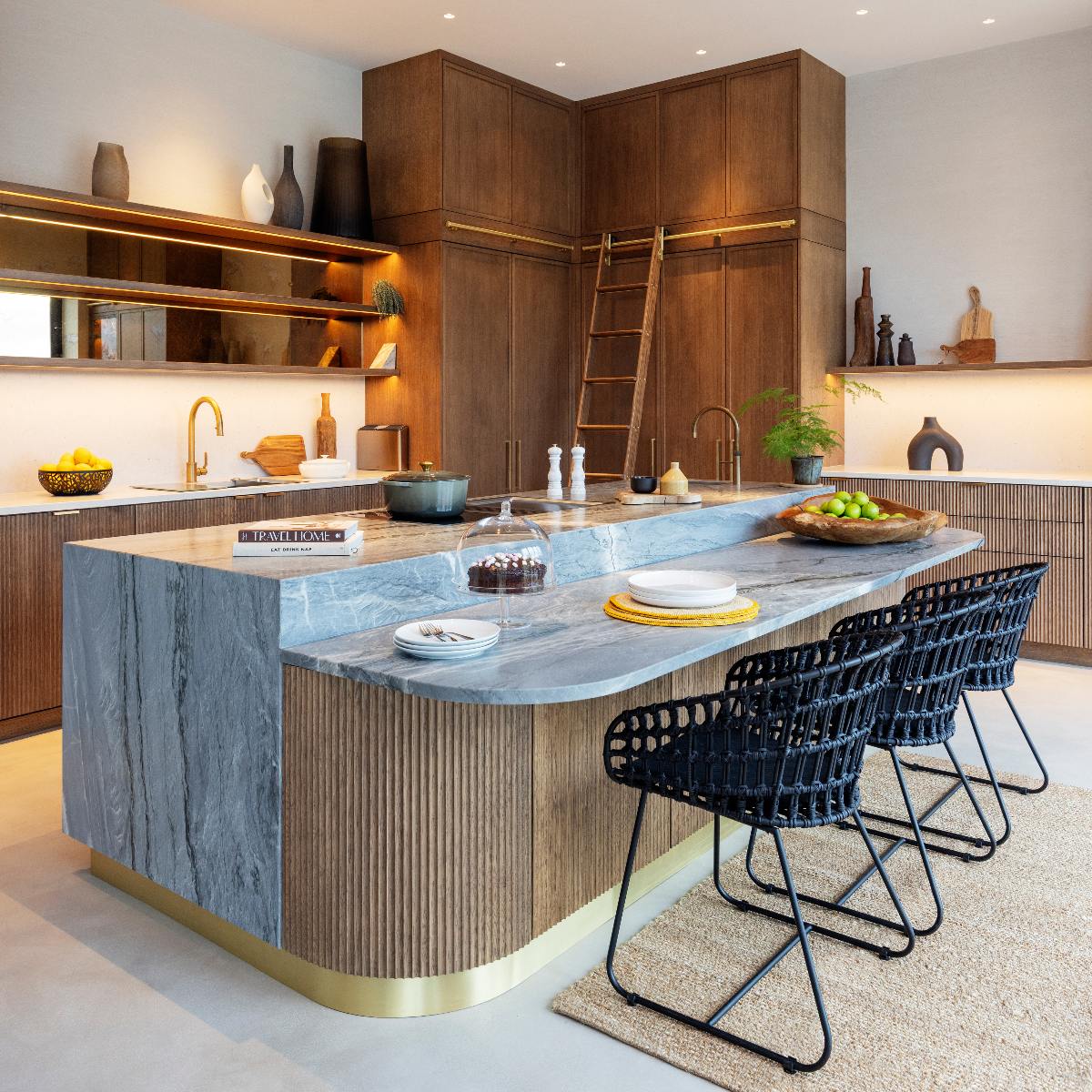 A wood kitchen with a living island that includes cooking appliances, a sink and tap, work surfaces, a breakfast bar and seating. 
