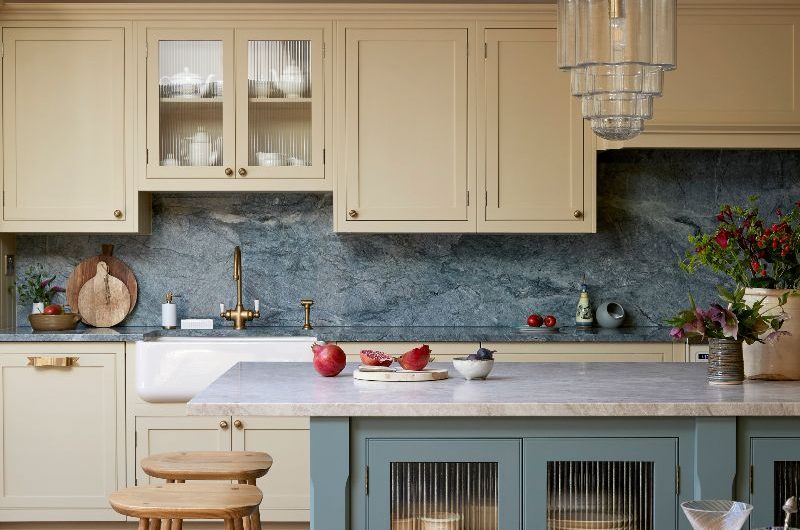 View of the Shaker kitchen with neutral run of cabinetry, a blue painted island, stone surfaces and wood flooring.