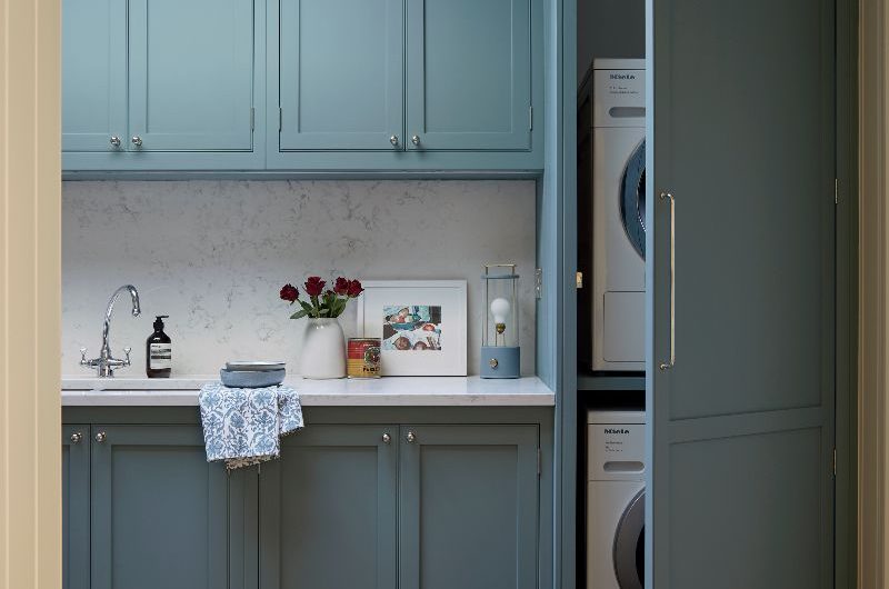 A utility room design with blue cabinetry, white veined surfaces, inset sink and chrome tap.