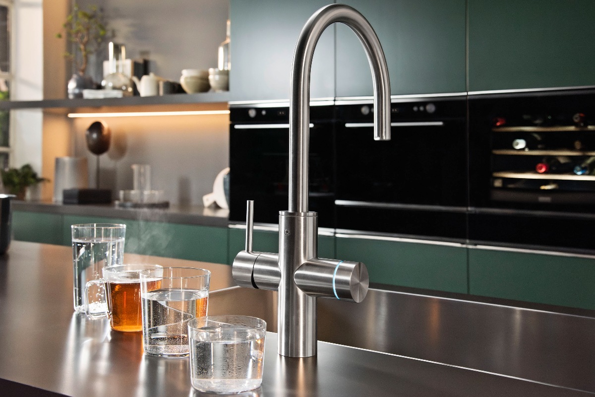 Dark green kitchen design for entertaining with built-in ovens, a boiling-water tap and stainless steel sink.