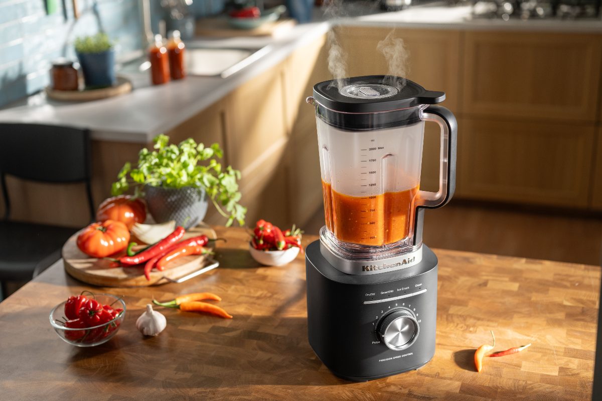 A sleek matte black soup maker with ingredients next to it in a wood kitchen.