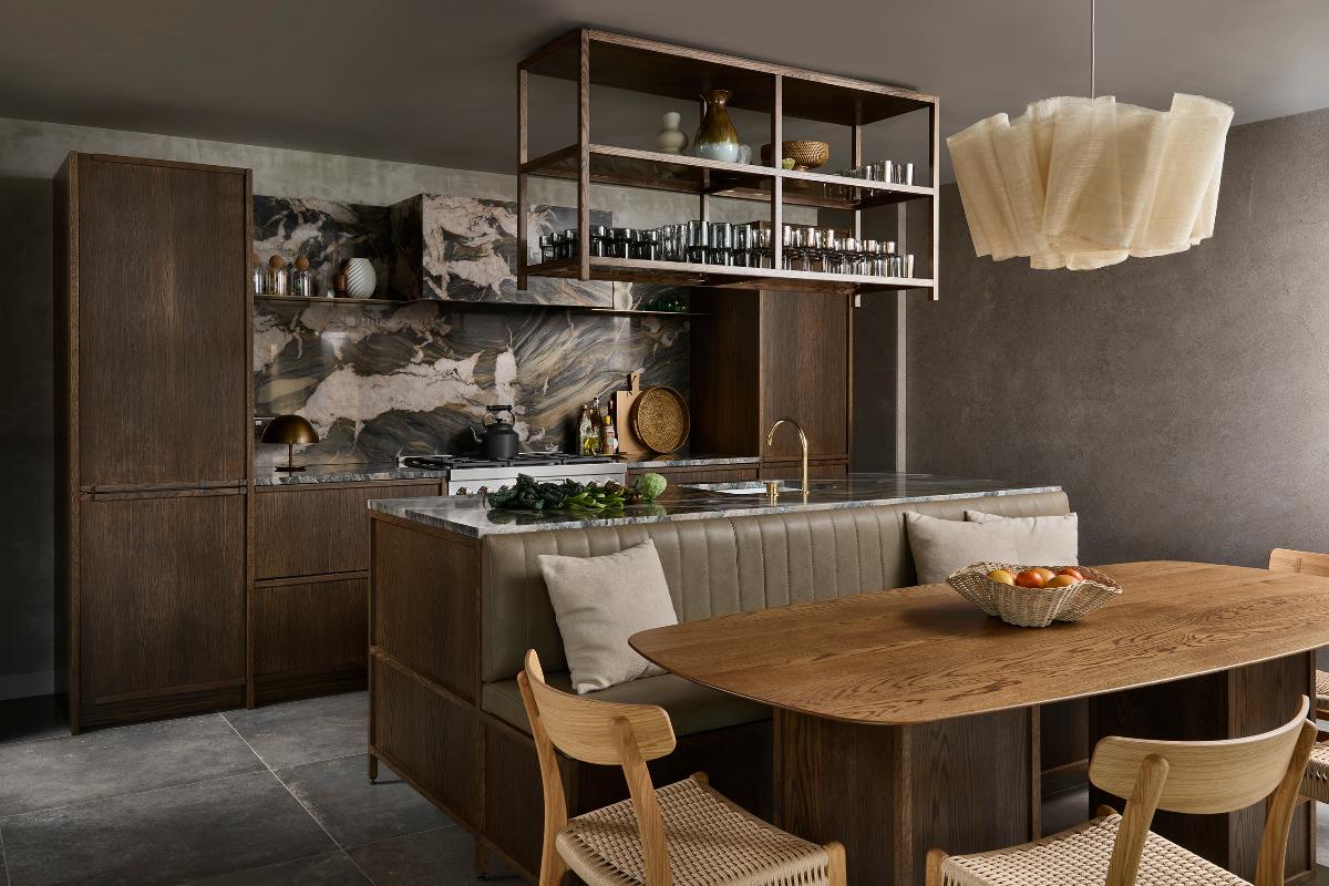 A modern design with dark stone surfaces, a multi-functional island with leather banquette seating, a wood table and chairs, and a hanging shelving unit above the working area.