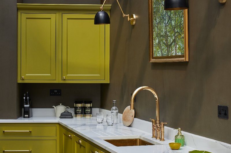 A zesty green kitchen design with terracotta flooring, brass details, and wall lights.