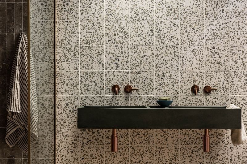 Bathroom clad in terrazzo with concrete basin, marbled floor. and aged brassware.