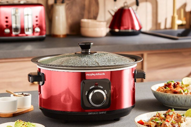 Autumn kitchen with a red slow cooker with meals served in glazed crockery, and matching kettle and toaster in the background.