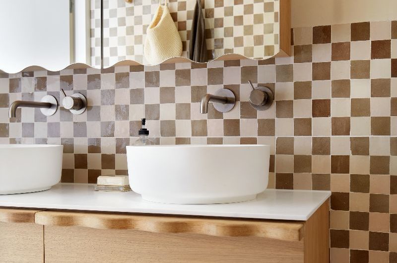 Vanity area with checkerboard tiles, mirror cabinet, wood furniture, white basins, and bronze brassware.