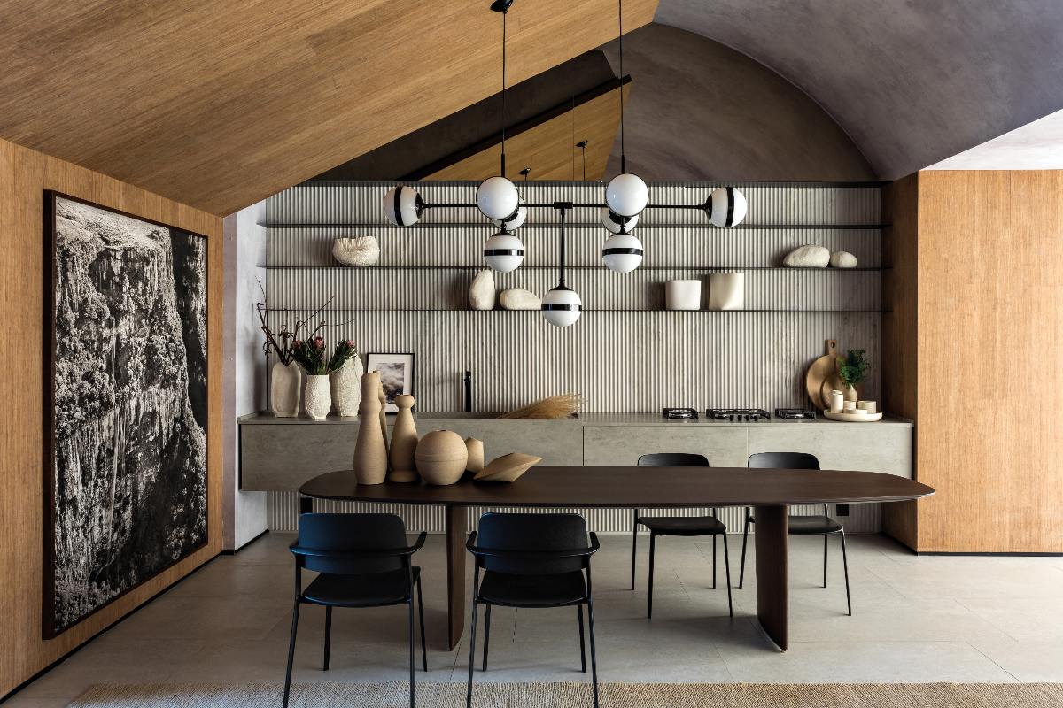 A one wall kitchen with open shelving for displaying art and crockery, with wood and concrete-effect surfaces, grey flooring, and a spacious dining area.