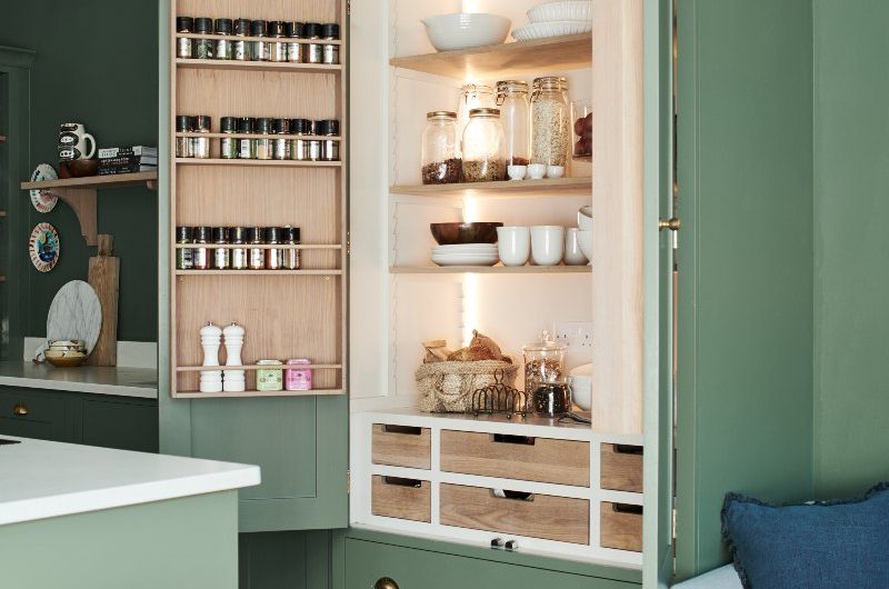 A green kitchen with a breakfast bar equipped with shelves, drawers, door racks and built-in lighting.