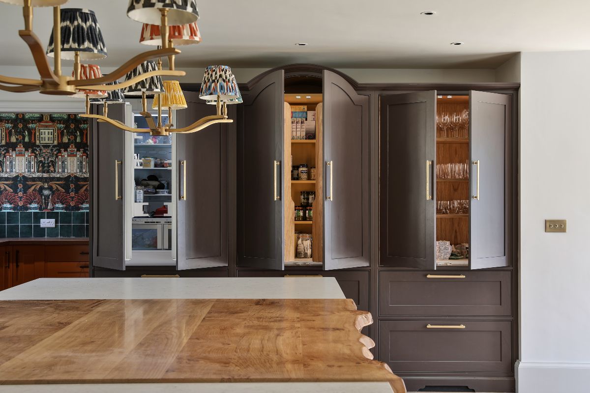 Open Shaker cabinets painted in a dark brown revealing a fridge, a pantry, and drinkware storage inside.