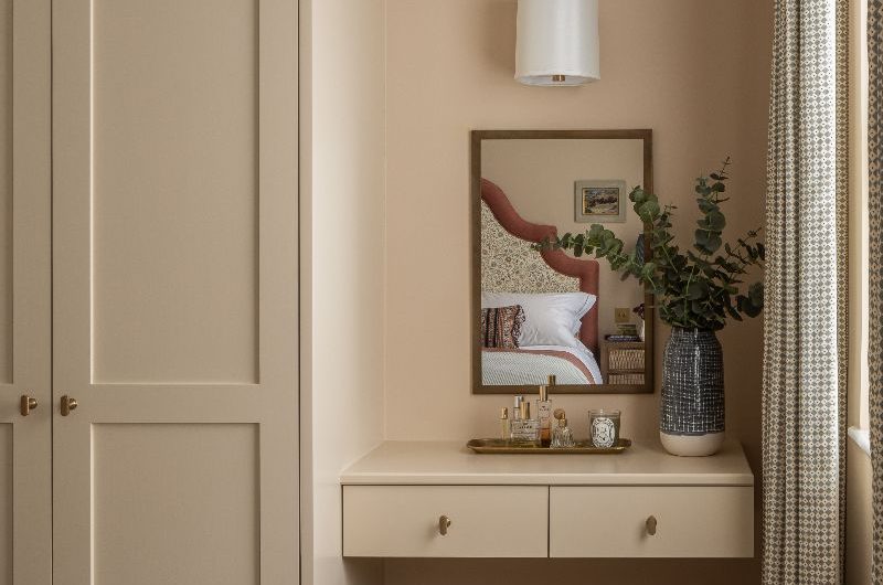A neutral bedroom design with a bijou dressing table, fitted wardrobes, and a boucle seat.