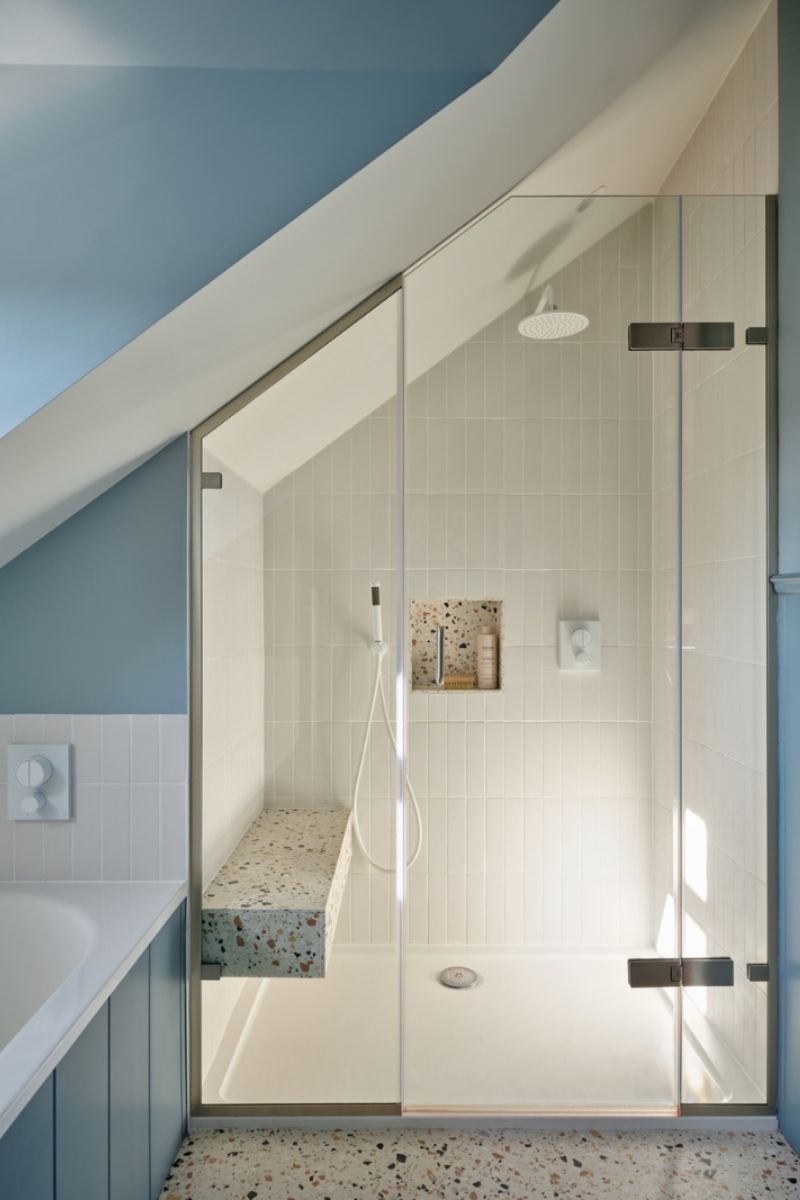 A boy's bathroom with a shower area which has a terrazzo seat, white brassware, and compact storage niche.