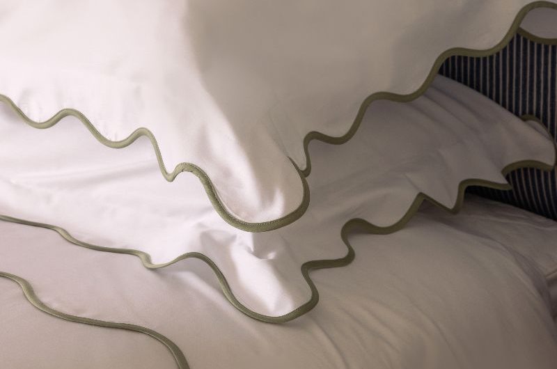 Closeup at white bedding with scalloped edges on a striped bed frame.